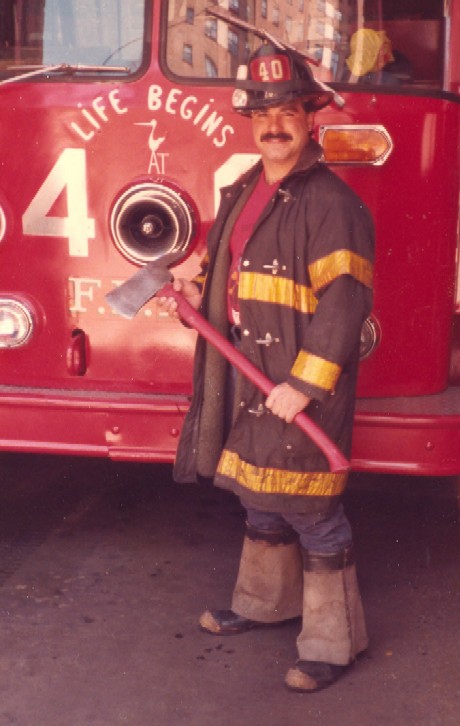 Lt. Chuck Margiotta in FDNY turnout gear, holding an axe in front of a fire truck
